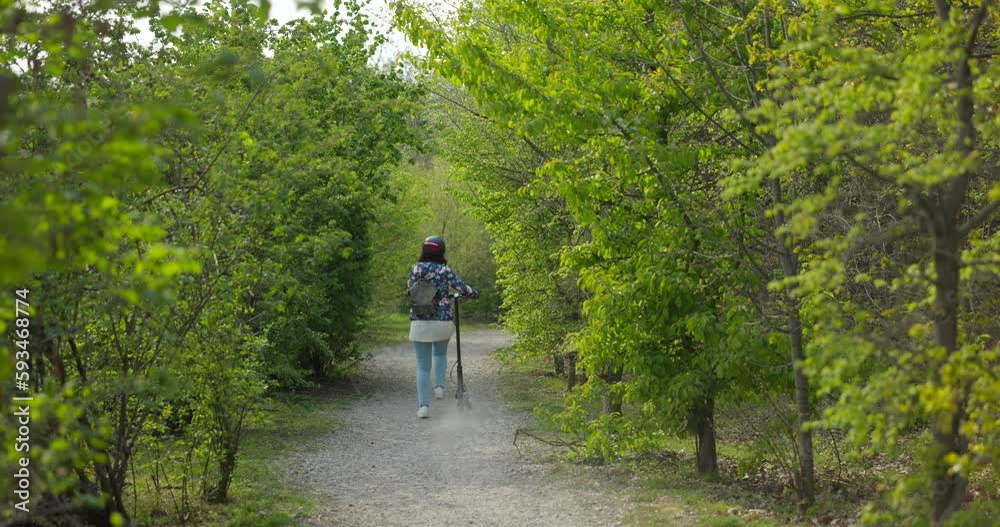 Woman on e-scooter rides by on gravel path through green bushes Woman on e-scooter rides by on gravel path through green bushes