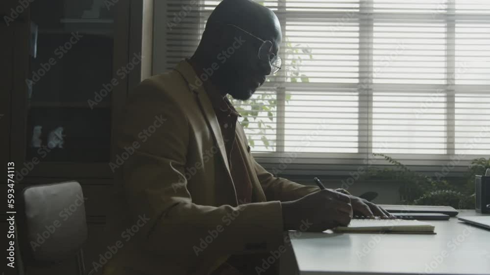 Psychologist sitting at desk writing in diary and checking the time