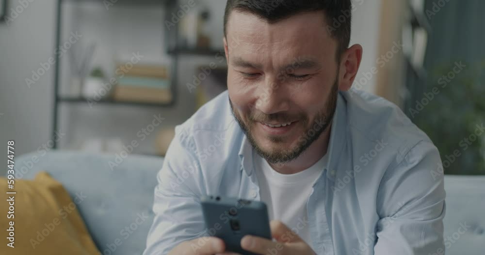 Carefree guy having fun with smartphone using device and smiling in leisure time at home. Electronics and enjoyable online content concept. Carefree guy having fun with smartphone using device and smiling in leisure time at home. Electronics and enjoyable online content concept.