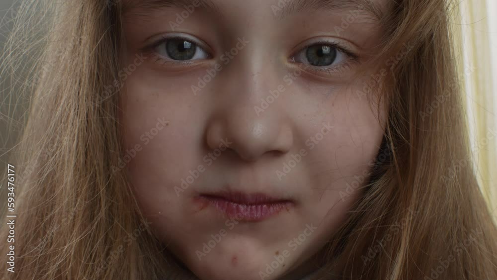 A cheerful girl with blond long hair eats a chocolate marshmallow. Close-up of a happy and contented girl's face eating chocolate-coated marshmallows. Happy childhood concept A cheerful girl with blond long hair eats a chocolate marshmallow. Close-up of a happy and contented girl's face eating chocolate-coated marshmallows. Happy childhood concept