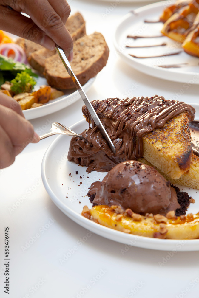 Chocolate french toast and banana slice served with chocolate gelato cutting with knife and fork in hand. 