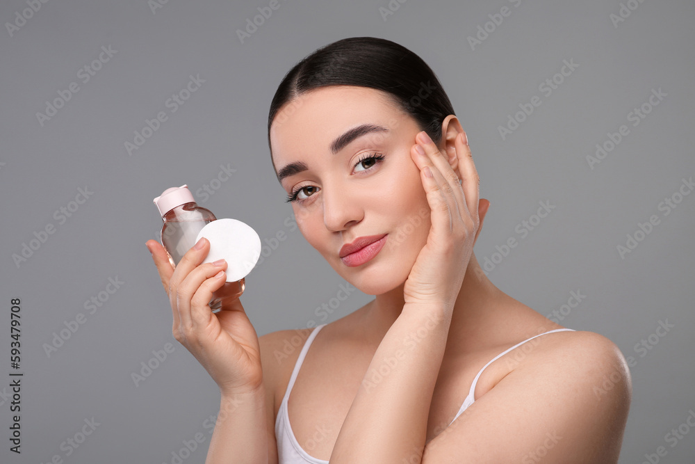 Beautiful woman with makeup remover and cotton pad on gray background Beautiful woman with makeup remover and cotton pad on gray background