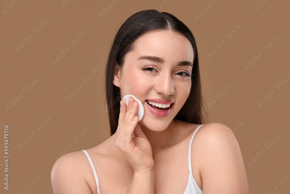 Beautiful woman removing makeup with cotton pad on beige background