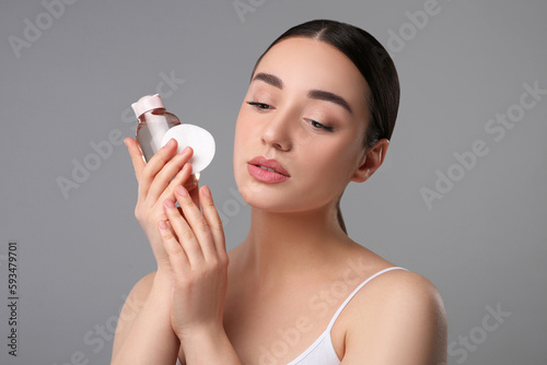 Beautiful woman with makeup remover and cotton pad on gray background