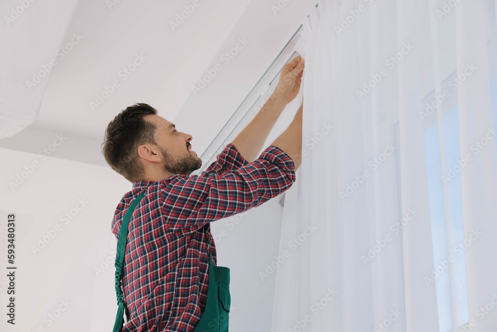 Worker in uniform hanging window curtain indoors, low angle view Worker in uniform hanging window curtain indoors, low angle view