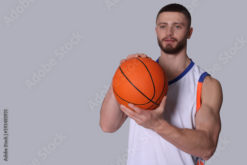 Athletic young man with basketball ball on light grey background. Space for text