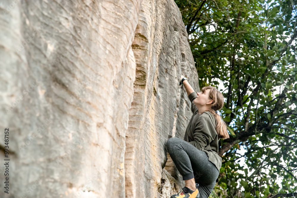 young active teen girl doing outdoor rock climbing bouldering on natural cliff