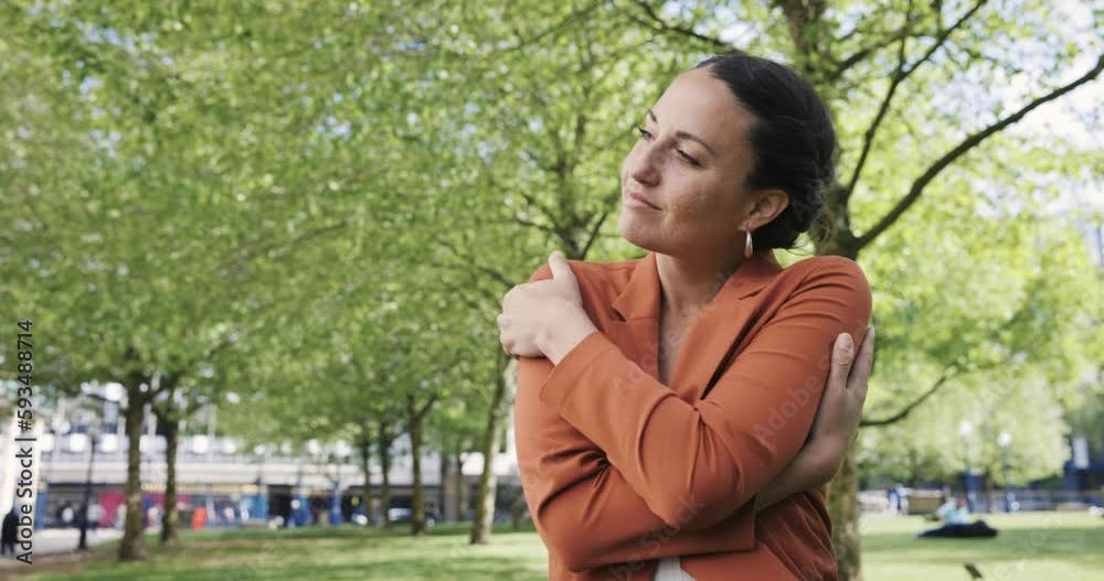 Woman standing in park hugging herself with eyes closed Woman standing in park hugging herself with eyes closed