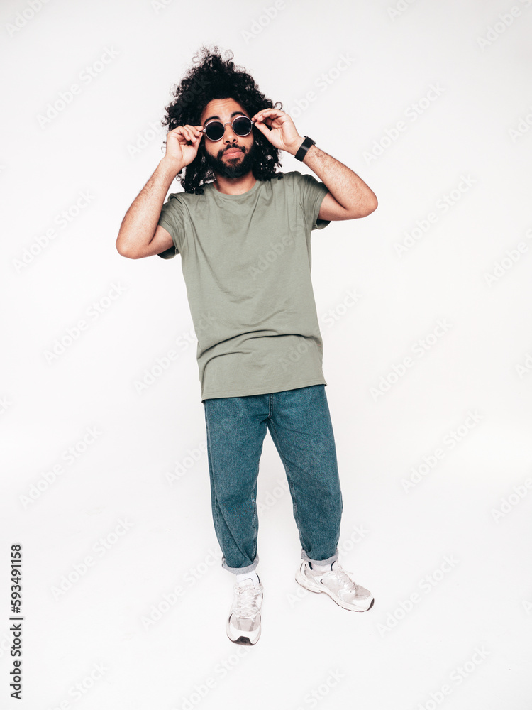Handsome smiling hipster model. Unshaven Arabian man dressed in summer t-shirt and jeans clothes. Fashion male with long curly hairstyle isolated on white in studio. Full length, in sunglasses Handsome smiling hipster model. Unshaven Arabian man dressed in summer t-shirt and jeans clothes. Fashion male with long curly hairstyle isolated on white in studio. Full length, in sunglasses