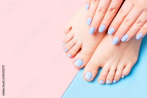 Female hands and feet with light blue manicure and pedicure on a blue and pink background top view close-up.