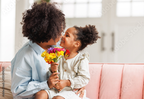 Photographie Happy mother's day! Afro american family happy child daughter congratulates mom on holiday, hugs her and gives bouquet of flowers
