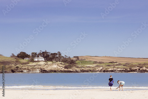Two young children beach combing along the shoreline near Padstow, Cornwall