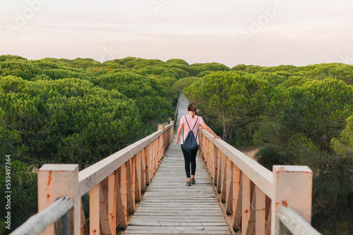 Backview of unknown woman walking across bridge in the middle of a forest at sunset