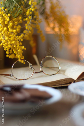 Cup of tea or coffee, plate of cookies, cup of blueberries, plate of chocolate, glass of juice, book, reading glasses, teapot, flowers and lit candles on the table. Brunch or afternoon tea concept.