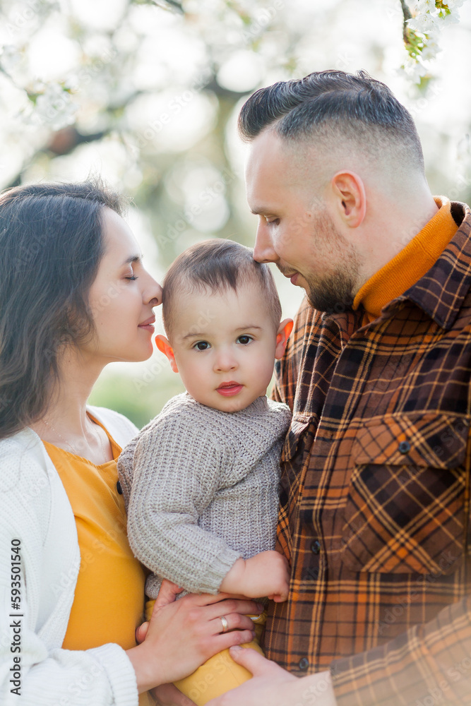 Happy young family with little son walks in blooming garden. Mom and dad with 1 year old baby. Spring. Happy young family with little son walks in blooming garden. Mom and dad with 1 year old baby. Spring.