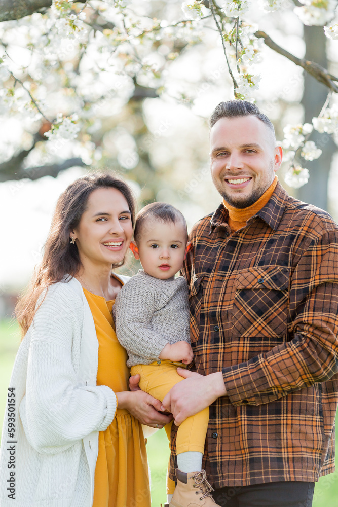 Happy young family with little son walks in blooming garden. Mom and dad with 1 year old baby. Spring. Happy young family with little son walks in blooming garden. Mom and dad with 1 year old baby. Spring.