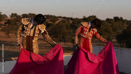 Two bullfighters dressed in the traditional matador costume practicing with the cape in the field at sunset