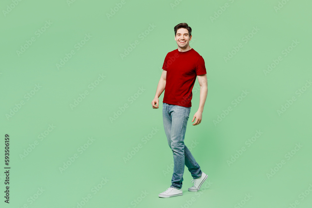 Full body side view happy young brunet caucasian man he wearing red t-shirt casual clothes walking going strolling isolated on plain pastel light green background studio portrait. Lifestyle concept. Full body side view happy young brunet caucasian man he wearing red t-shirt casual clothes walking going strolling isolated on plain pastel light green background studio portrait. Lifestyle concept.