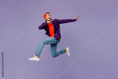 Full body side view young man of African American ethnicity wears casual shirt orange hat jump high run fast with outstretched hands isolated on plain pastel purple color background studio portrait.