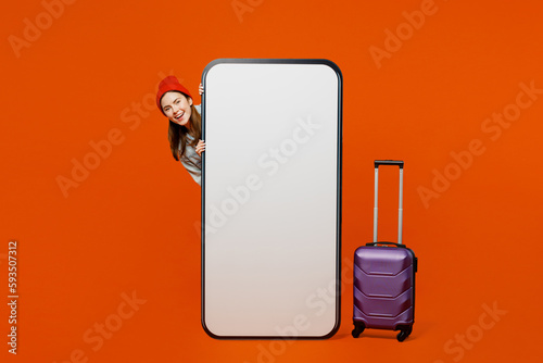 Traveler woman in casual clothes hold suitcase big huge blank screen mobile cell phone isolated on plain red orange background Tourist travel abroad in free time rest getaway Air flight trip concept #593507312