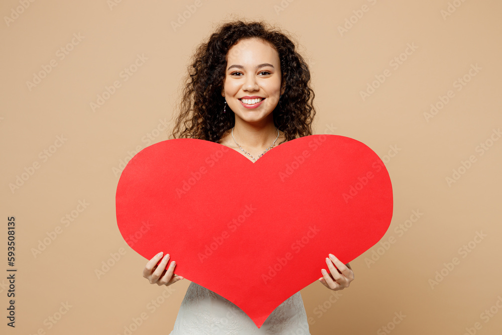 Happy beautiful fun young woman bride wear wedding dress posing hold in hands big red heart mockup isolated on plain pastel light beige background studio portrait. Ceremony celebration party concept. Happy beautiful fun young woman bride wear wedding dress posing hold in hands big red heart mockup isolated on plain pastel light beige background studio portrait. Ceremony celebration party concept.