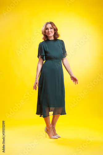 Elegant fashion. Stunning woman in elegant long dress in studio stands on a yellow sunny background.