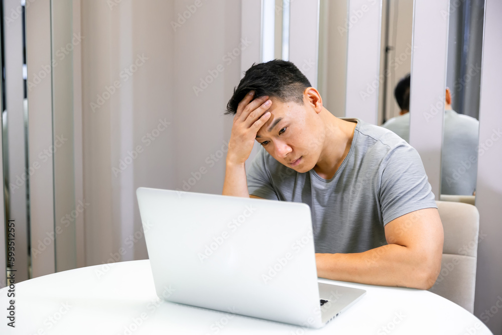 Young businessman tired of the computer, sitting at a table at home with a laptop, holding his head from a headache Young businessman tired of the computer, sitting at a table at home with a laptop, holding his head from a headache