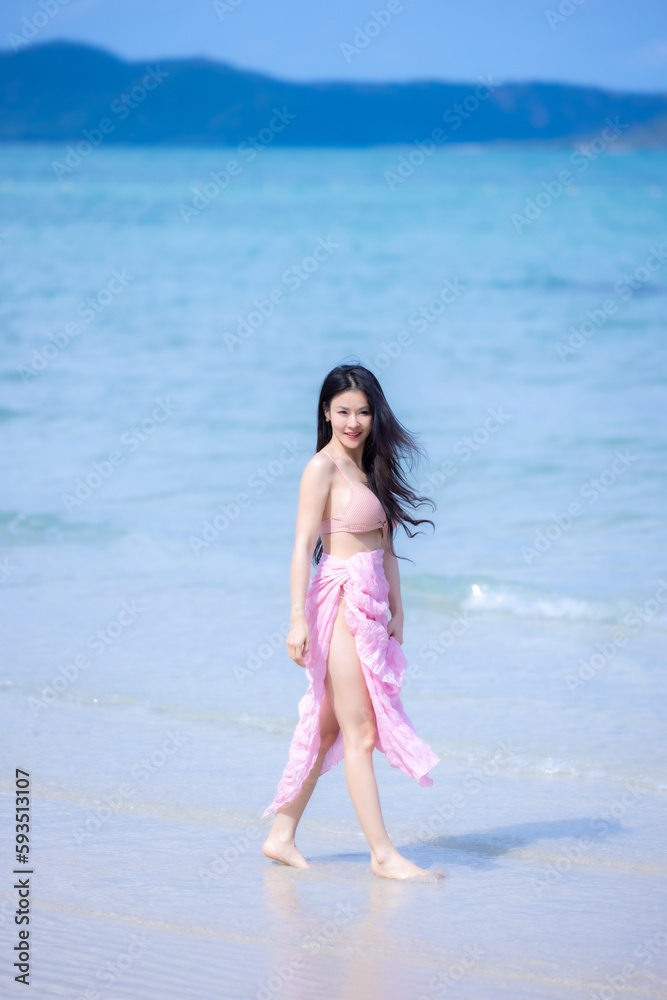 Beautiful woman relax and walking on sandy beach near waving foamy sea. Woman traveler smiling and walks barefoot on the beach. Young woman happy in walks along seashore. Summer vacation concept. Beautiful woman relax and walking on sandy beach near waving foamy sea. Woman traveler smiling and walks barefoot on the beach. Young woman happy in walks along seashore. Summer vacation concept.