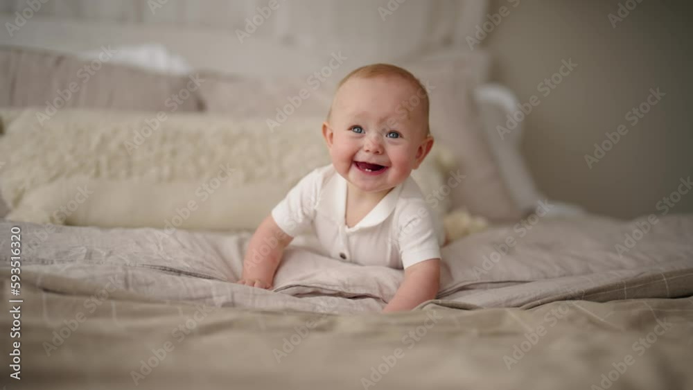 Happy laughing active healthy baby lying in bed trying to crawl waving hand at home. Portrait of adorable little kid having good mood. Rising son, first steps in crawling after hand plank, babycare. Happy laughing active healthy baby lying in bed trying to crawl waving hand at home. Portrait of adorable little kid having good mood. Rising son, first steps in crawling after hand plank, babycare.