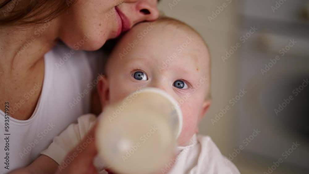 Mom feeding baby using bottle with milk mix kissing son to head. Mother