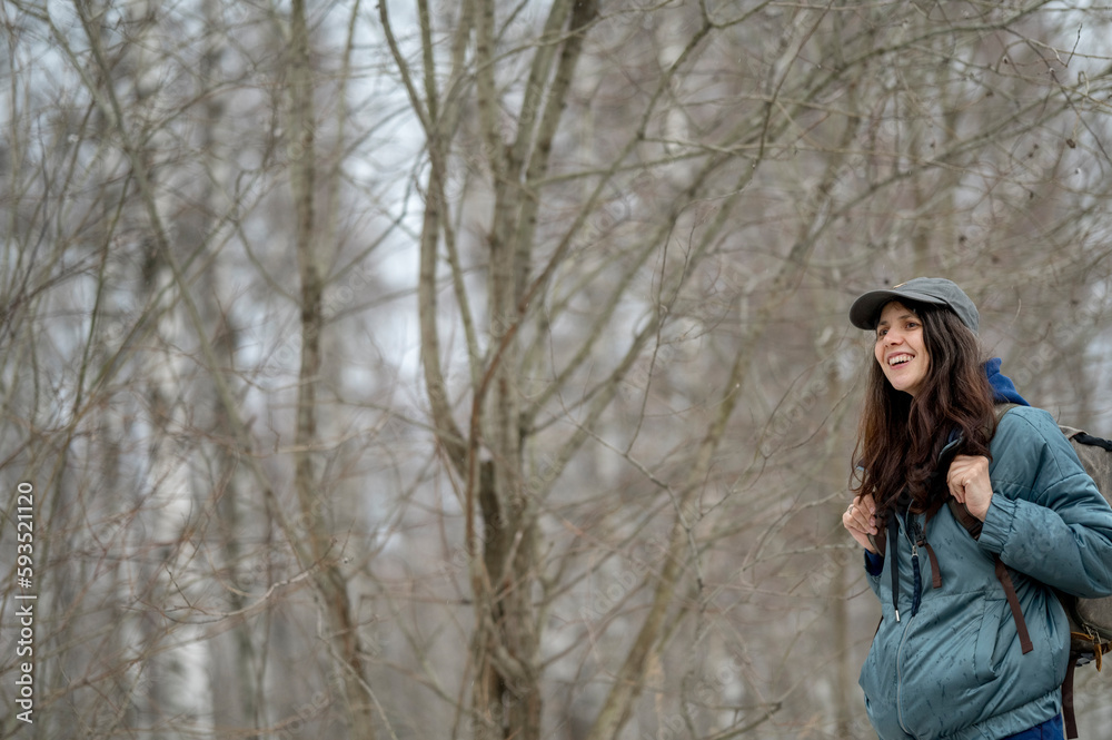 Happy woman wearing cap standing in front of bare trees in forest Happy woman wearing cap standing in front of bare trees in forest