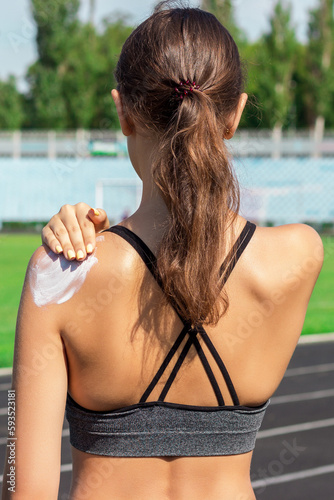 Sunscreen sunblock. Woman in a sportswear putting solar cream on shoulder on beautiful summer day. Sporty woman applying sunscreen on sport stadium. Sports and healthy concept