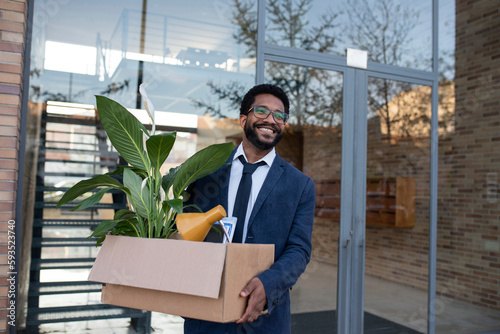 Smiling businessman leaving office building carrying cardboard box photo