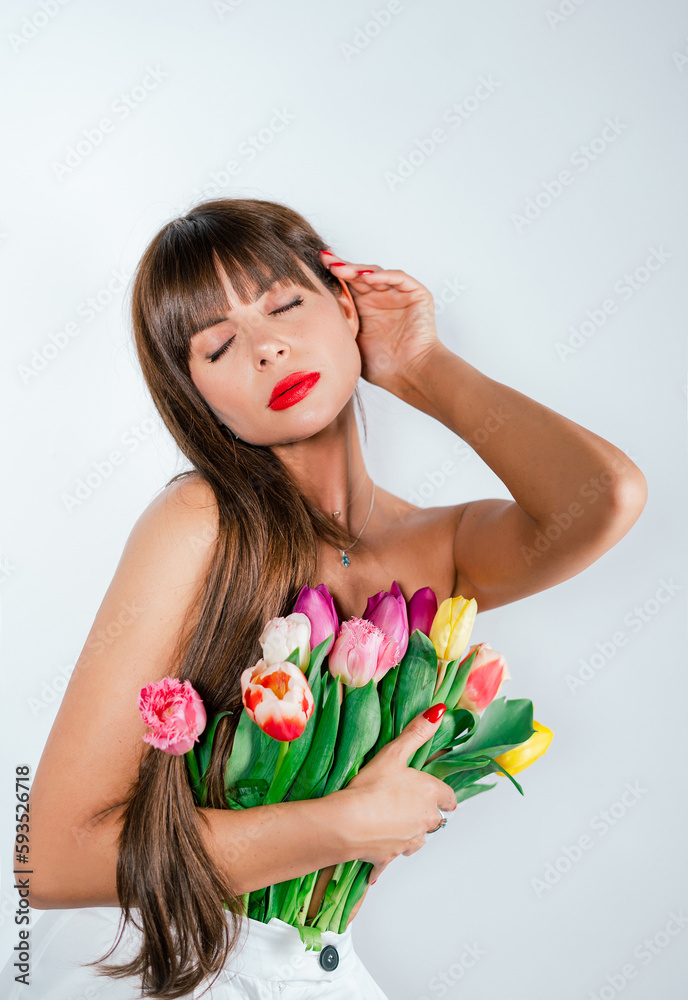 Fototapeta premium A slender girl presses flowers to her bare chest. Beautiful girl with a bouquet of tulips isolated on white background