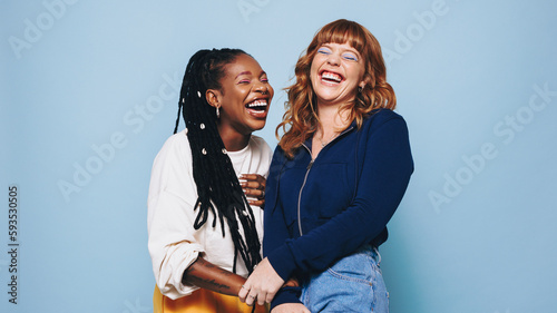 Fotografia Funny best friends laughing cheerfully while standing together in a studio