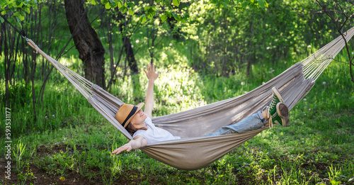 Young happy caucasian woman in a hat lying in a hammock in a green garden enjoying a summer day photo