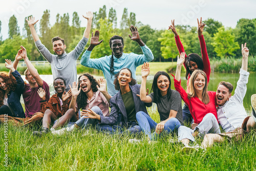 Multiethnic friends celebrating together while sitting on grass outdoor - Focus on center girl face