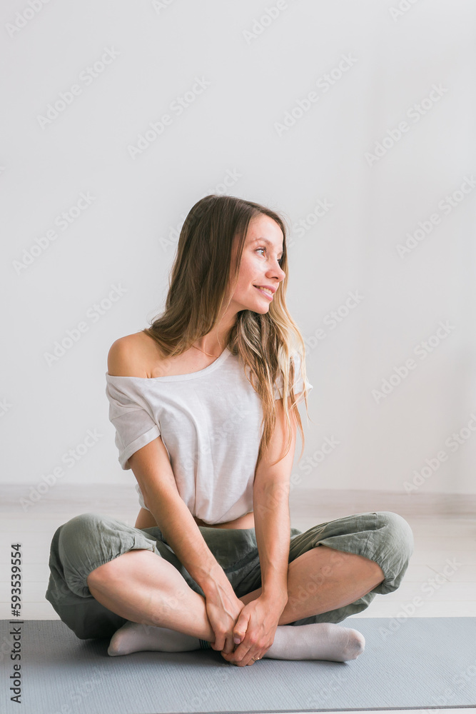 Positive girl sitting on fitness mat resting after pilates or yoga practice. Mindfulness and wellbeing concept. Positive girl sitting on fitness mat resting after pilates or yoga practice. Mindfulness and wellbeing concept.