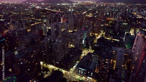 Illuminated futuristic night time Santiago, Chile high rise cityscape aerial view flying over diverse old and modern skyscraper capital