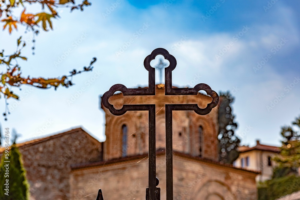 Closeup of metal cross and church with blue cloudy sky in the background