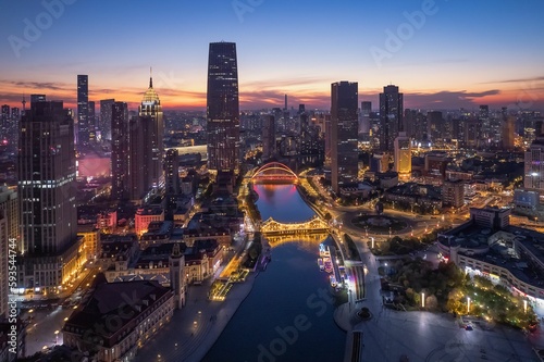 Drone modern cityscape view with a river and illuminated buildings at sunset