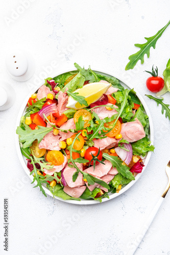 Canned Tuna salad with colorful cherry tomatoes, red onion, sweet corn, paprika, lettuce, radicchio and arugula. White table background, top view