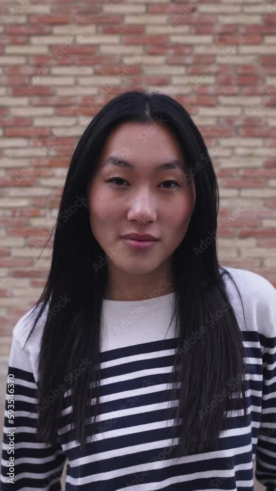 Vertical portrait of happy young asian woman smiling at camera standing over brick background wall. Chinese people concept