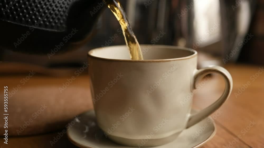 Pouring hot tea from teapot in cup at kitchen