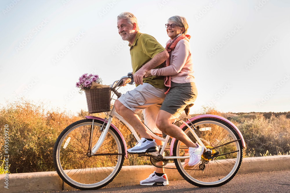 Fototapeta premium Healthy ad active mature retired people lifestyle. Man carrying woman senior aged on the same bike. Retired people having fun in outdoor leisure activity. Togetherness concept life. Happiness youthful