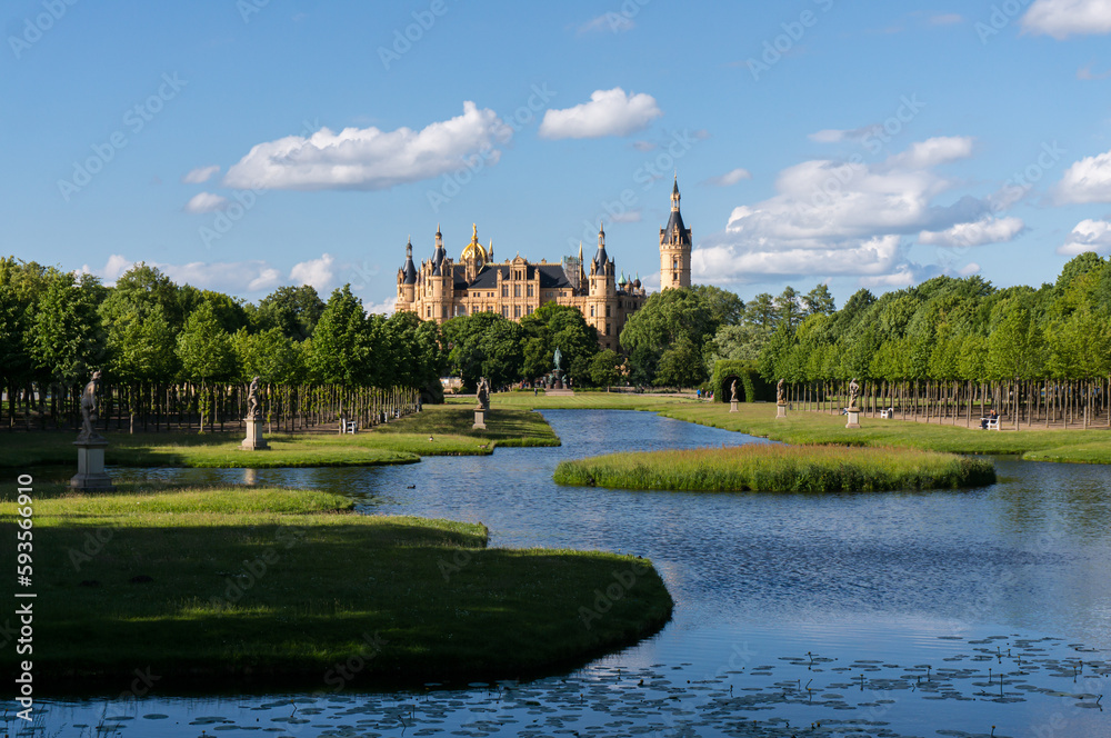 Obraz premium View through the palace gardens towards Schwerin Palace. Reflection in the water. Sunny day with light clouds.