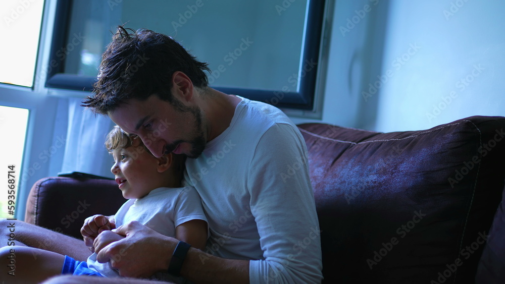 Father and son sitting on couch bonding together. Fatherhood lifestyle relationship. Dad embracing child indoors