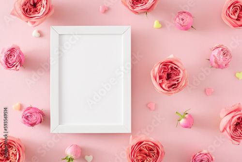 Flat lay photo of empty photo frame and natural flowers pink rose buds and small hearts on isolated pastel pink background. Mother Day atmosphere concept