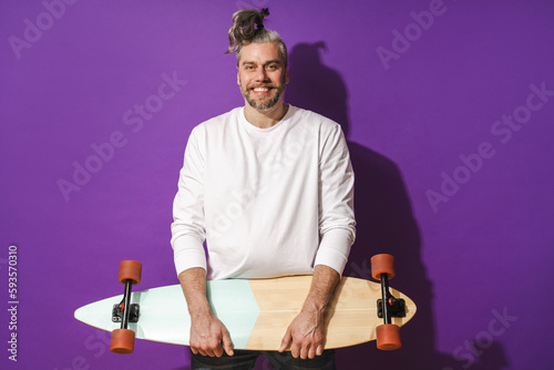 Cheerful middle aged man with longboard wearing white sweatshirt against purple background