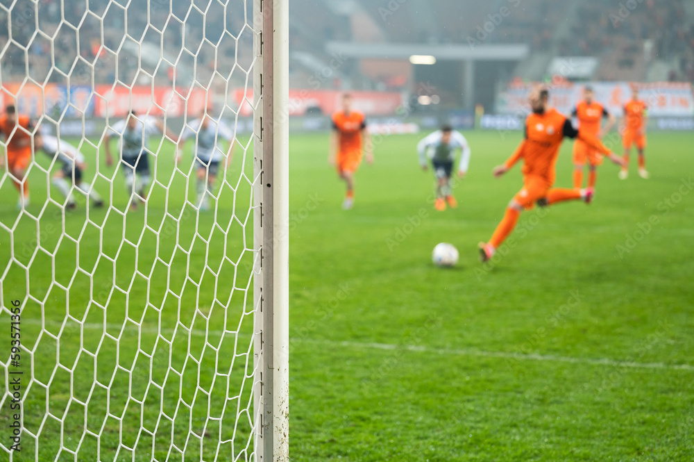 Detail of goal's post with net and football player during penalty kick in the background.